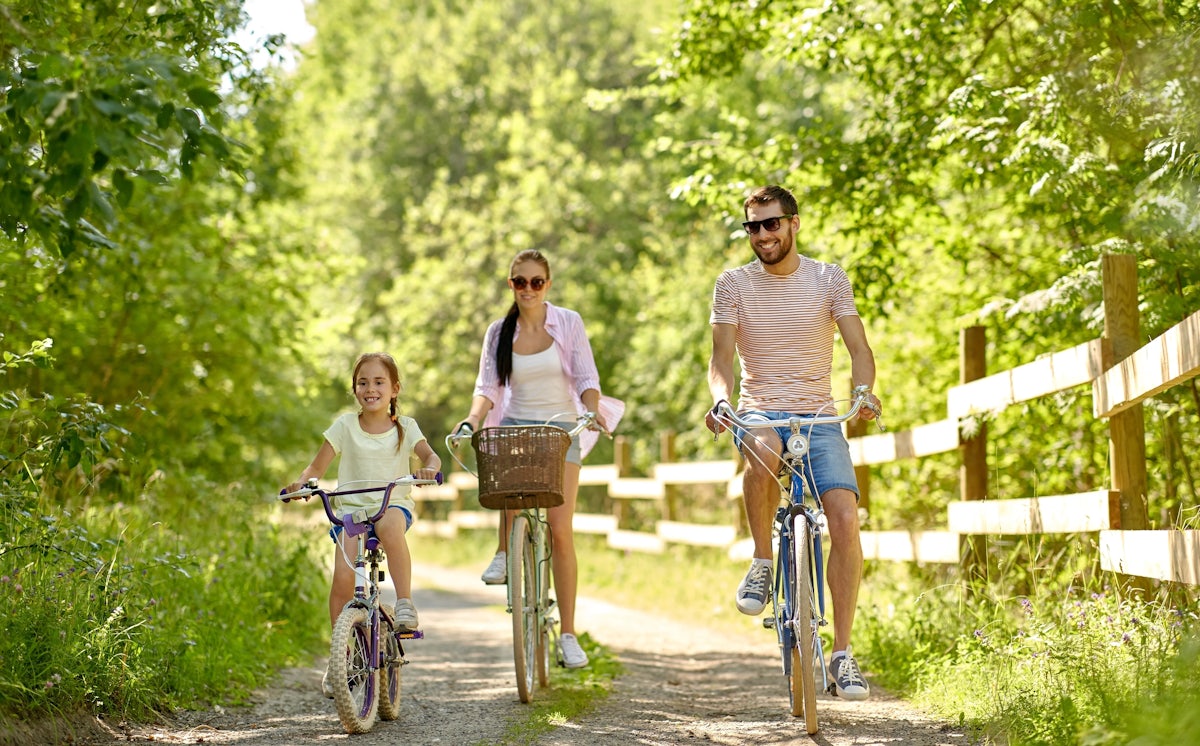 Family of three biking on a forest trail with a wooden fence on the side