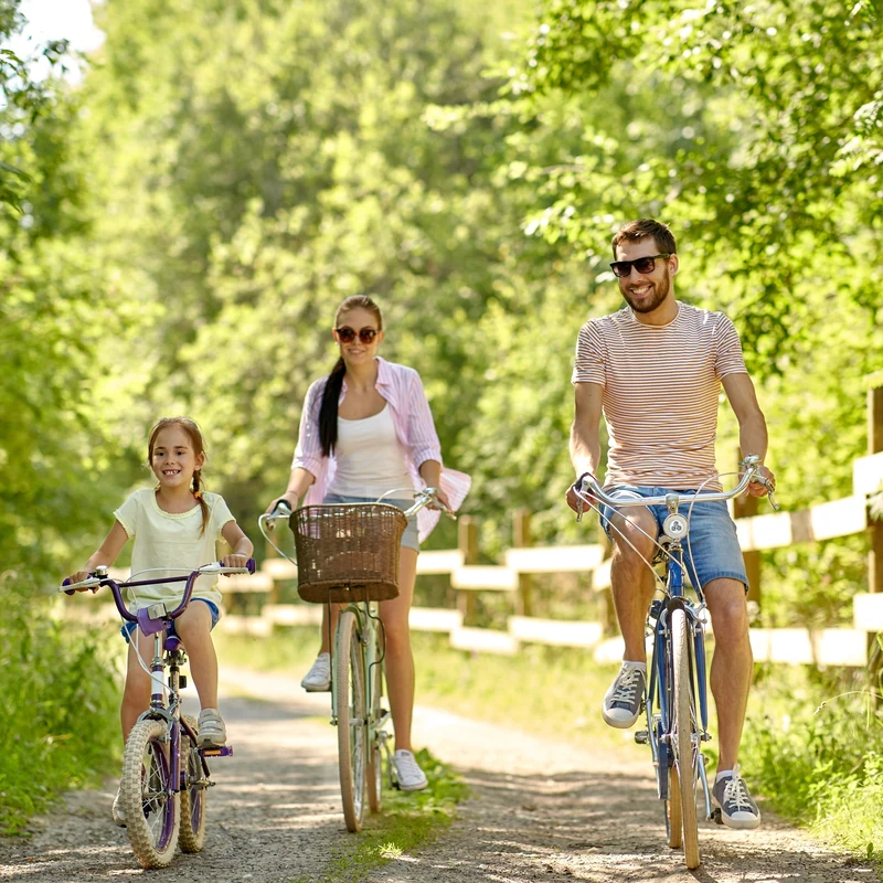 Family of three biking on a forest trail with a wooden fence on the side